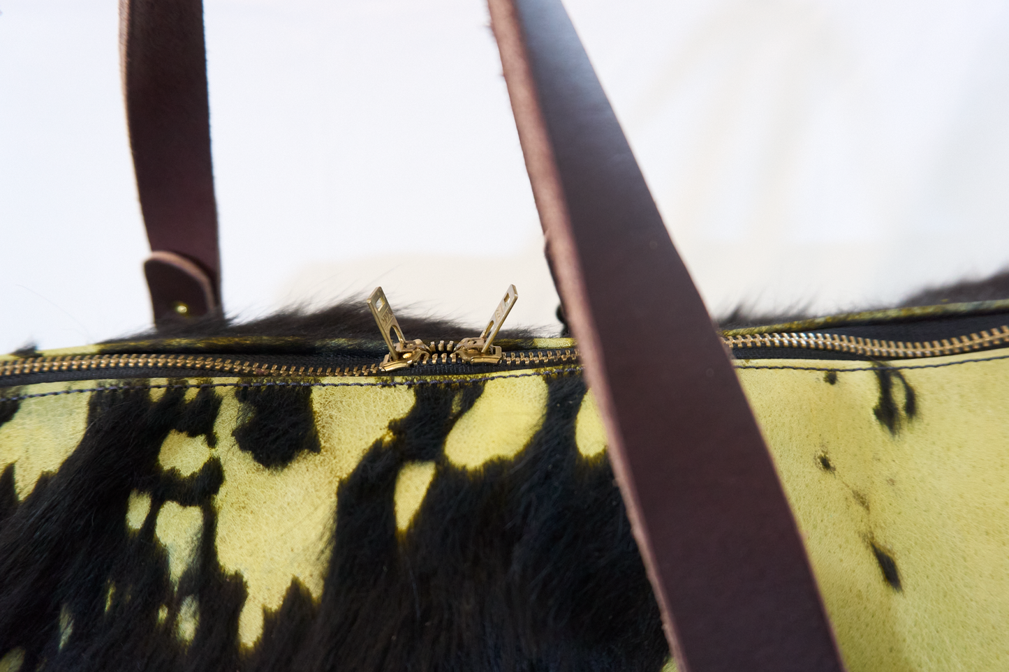 Closeup of zipper pulls on a bright green duffle bag made from hair-on cow leather.