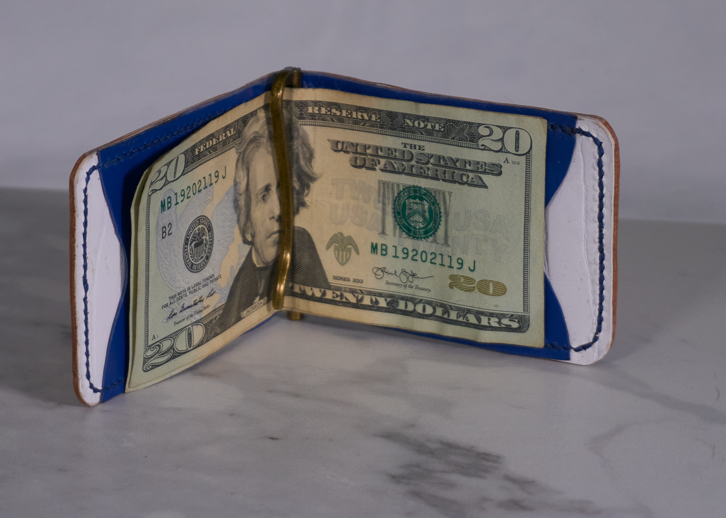 Interior of money clip with white kangaroo lining, blue kangaroo card pockets, and brass money clip with cash