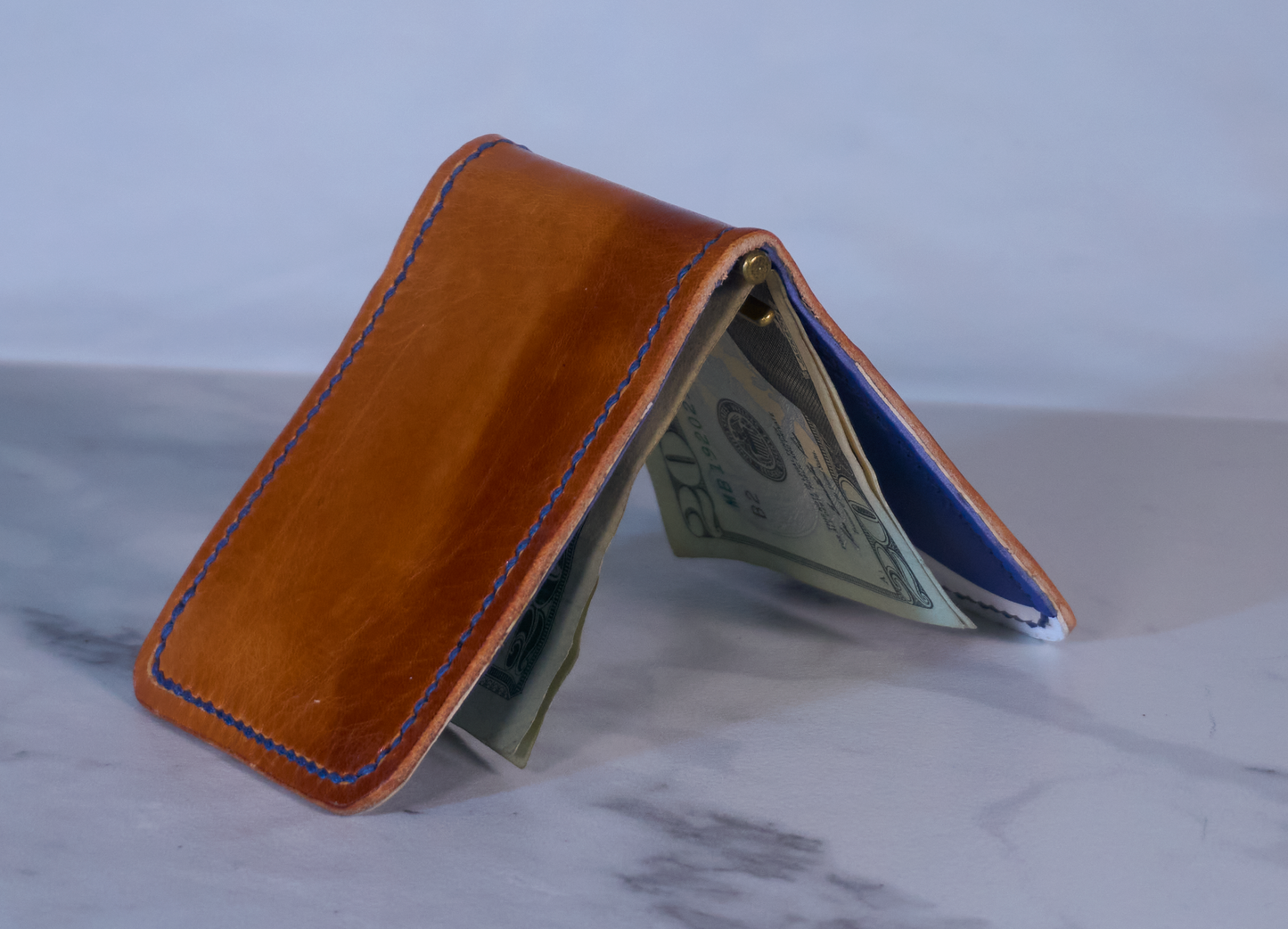Tent view of money clip with orange exterior showing white lining and blue card pockets with cards and cash