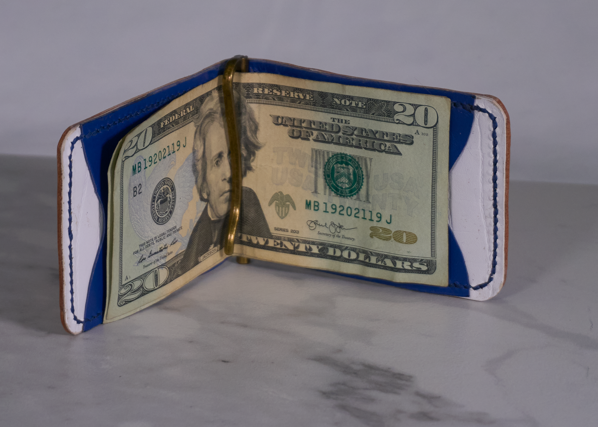 Interior of money clip with white kangaroo lining, blue kangaroo card pockets, and brass money clip with cash