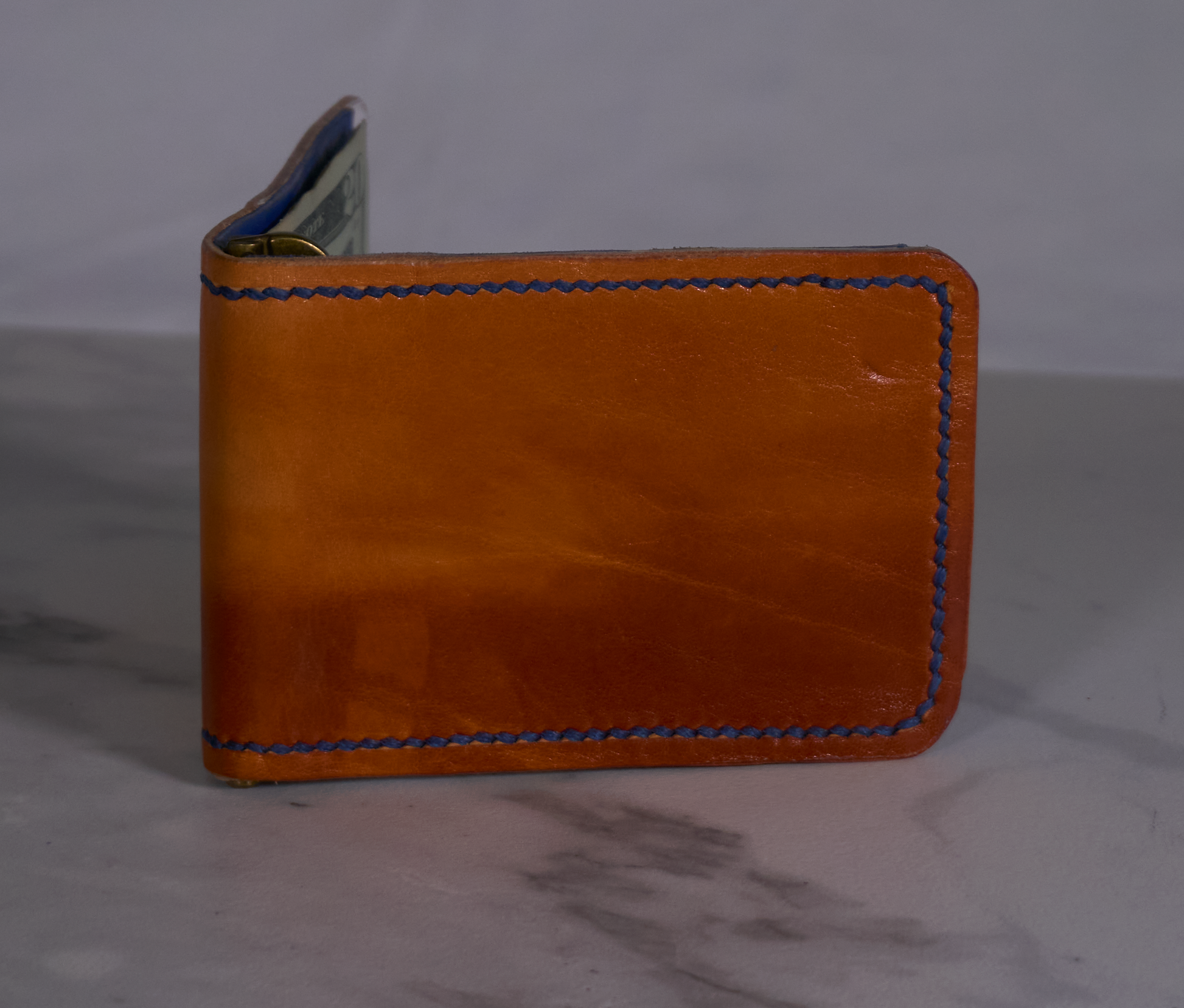 Exterior of orange money clip showing white lining, blue card pockets, and cash with a brass money clip